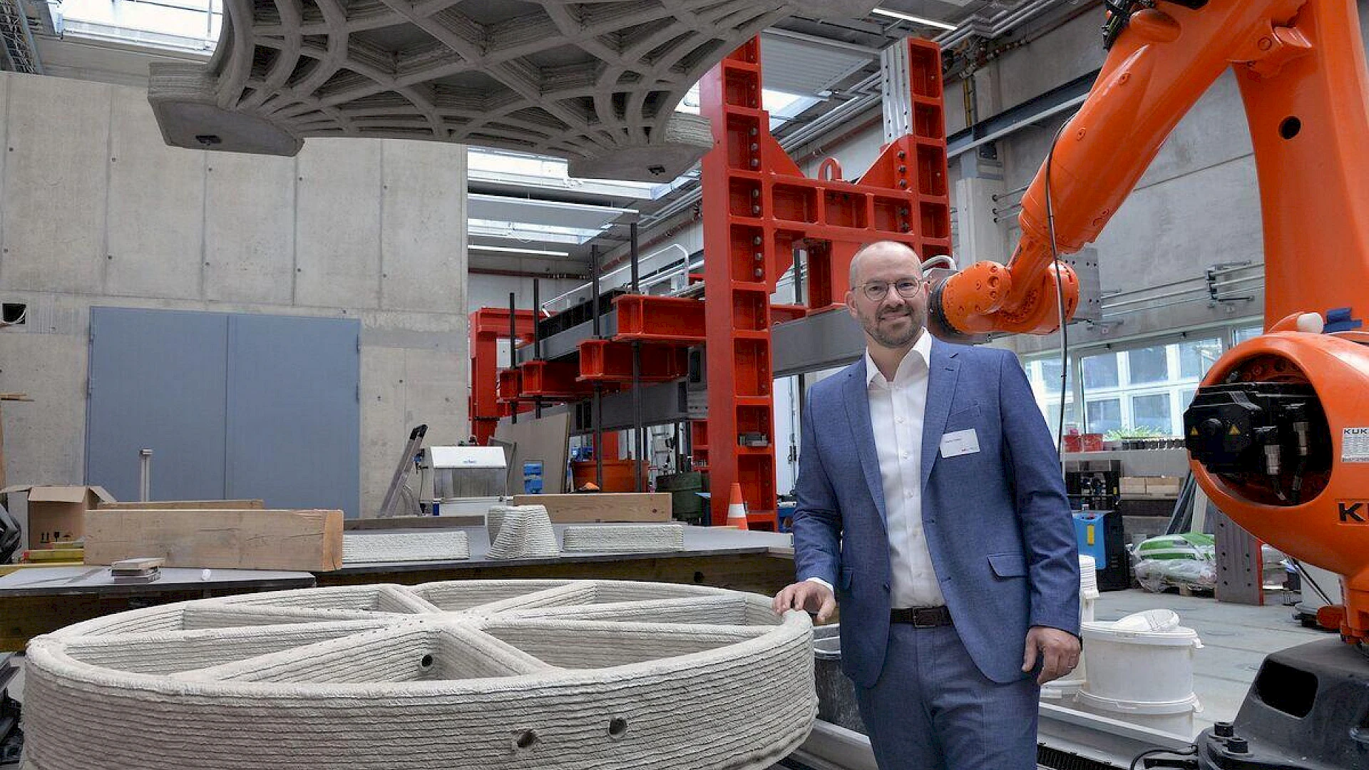 Professor Martin Claßen at the laboratory of the Instuitute of Structural Concrete. A person in a laboratory in front of a industrial robot and a concrete 3d-printed component