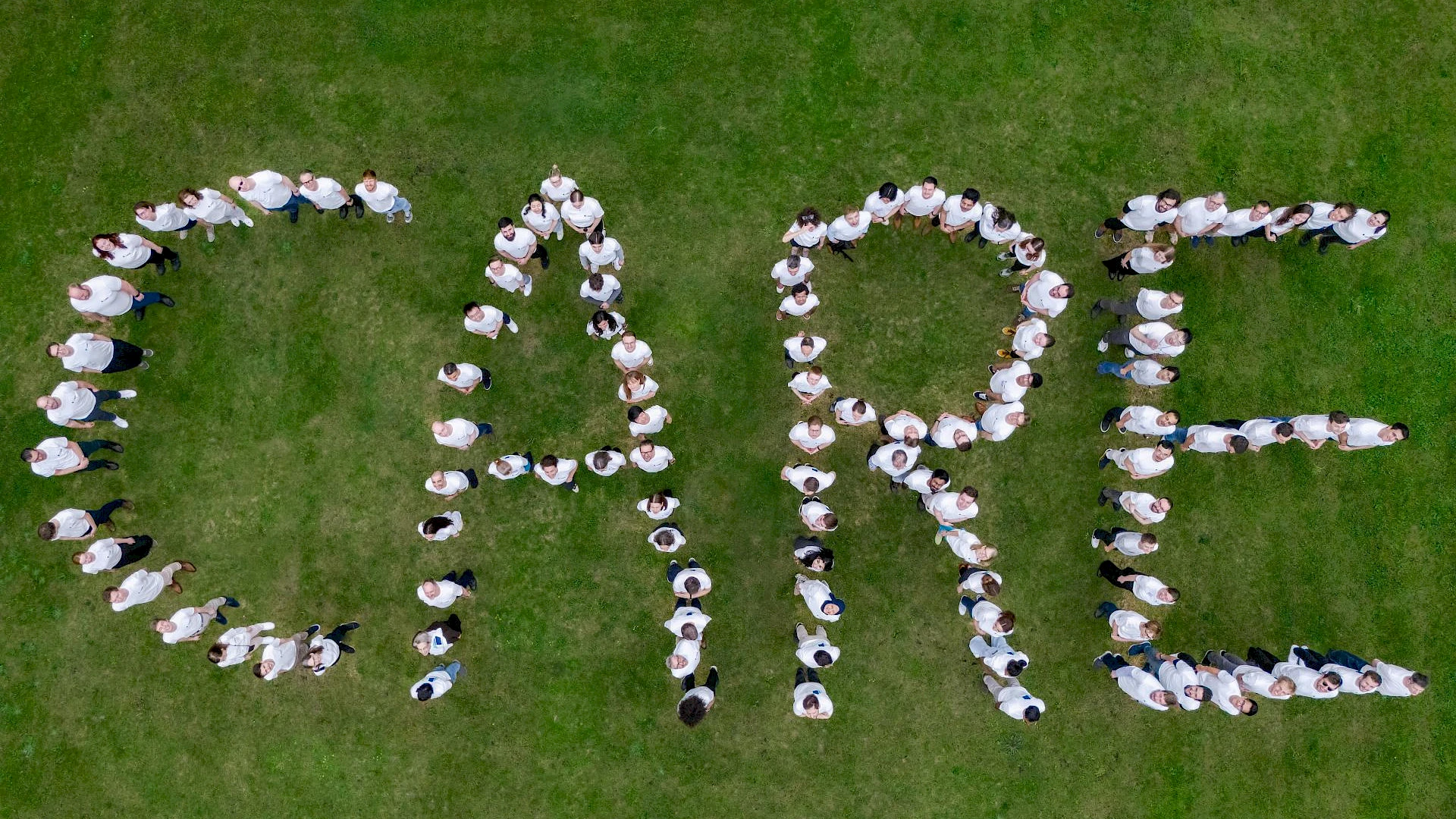 a group of people on a lawn forming the letters "CARE" with their bodies
