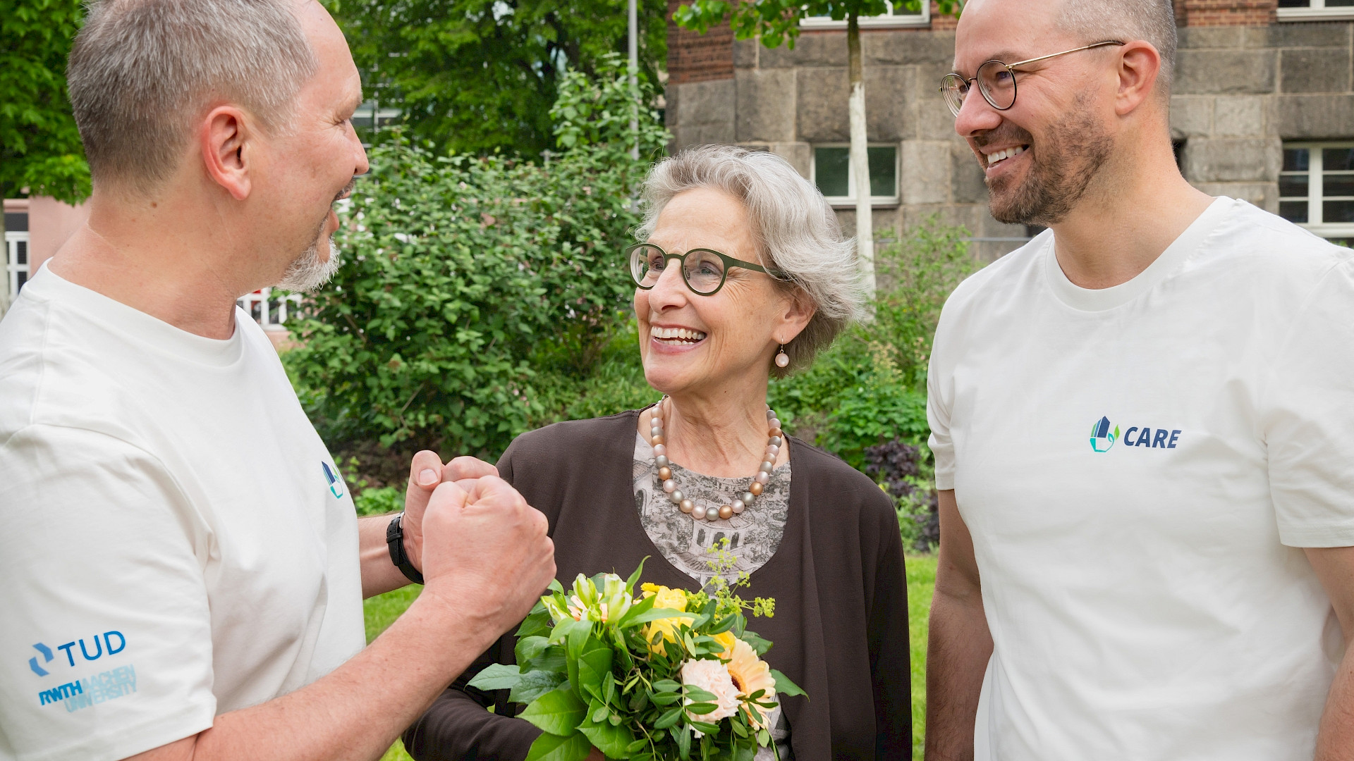Two man in white shirts talking to a woman with flowers in her hand