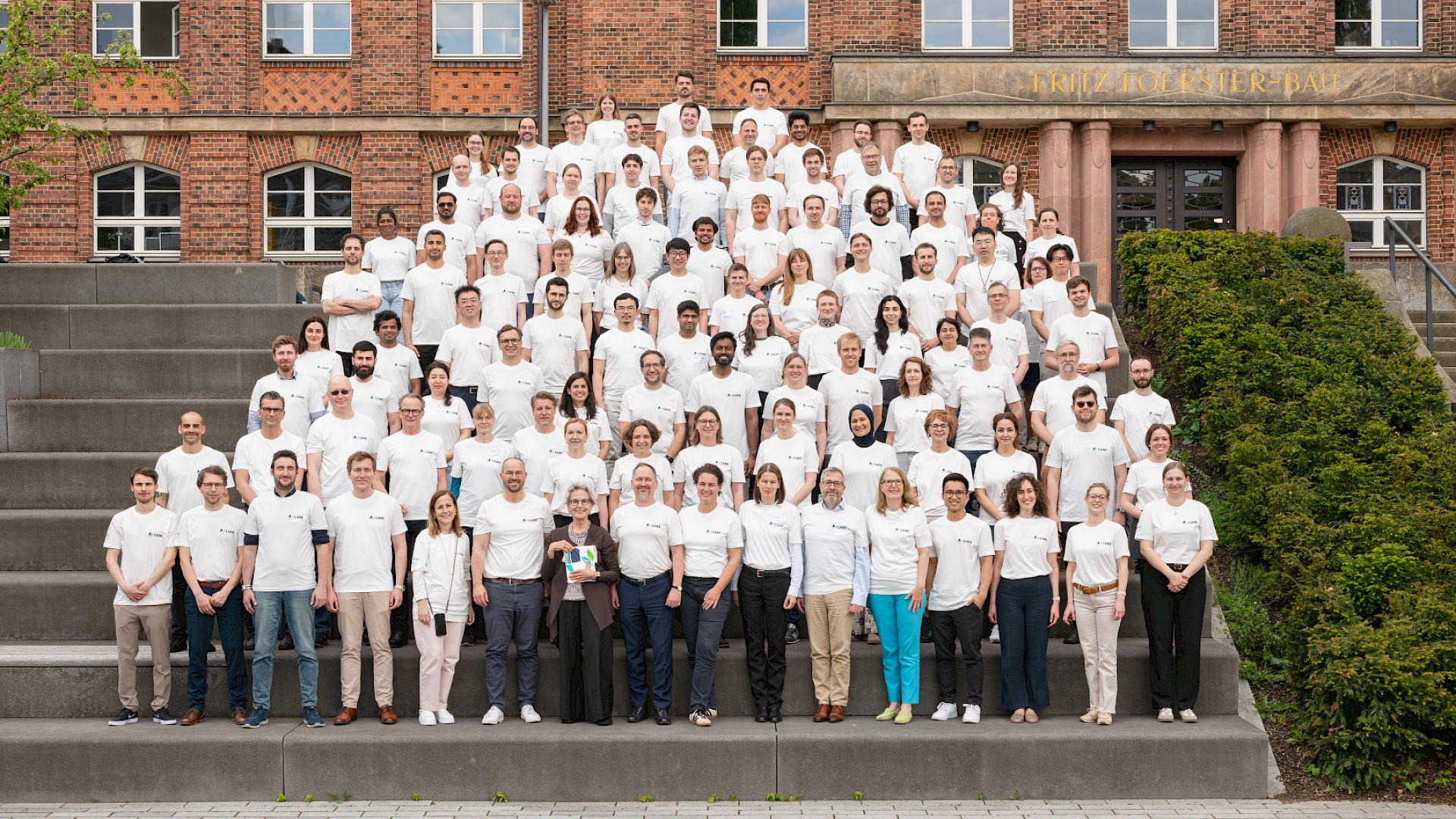 The CARE team, with all its members, at the cluster’s first annual general meeting in 2026. A group photo of people, all with the same white t-shirt on a big staircase in front of a brick building