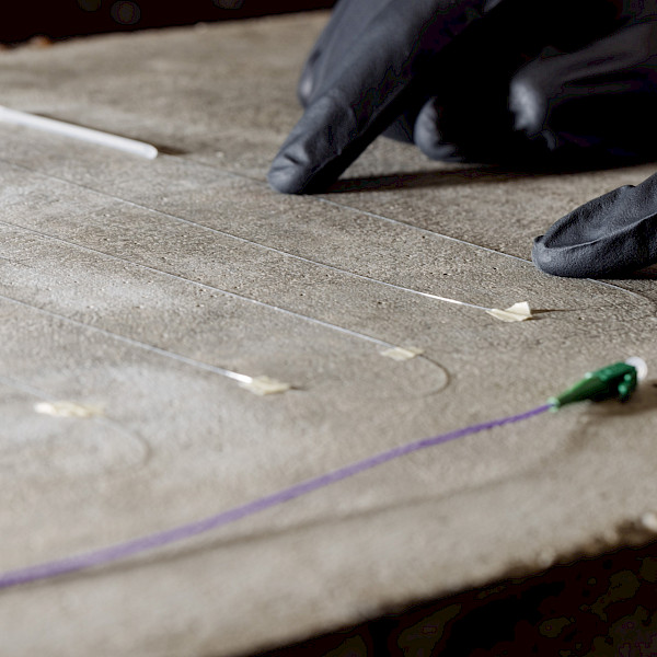 Application of fibre-optic measurement technology for the continuous monitoring of strains and cracks on a concrete surface. Installation of fibre-optic measurement technology on concrete for the continuous monitoring of strains and cracks.